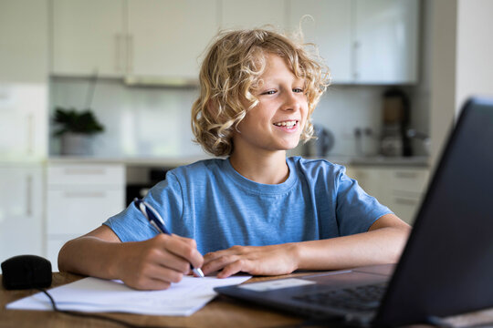 Happy boy doing homework watching laptop at home