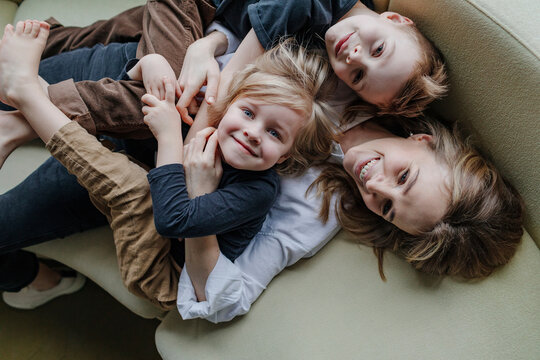 High angle view of happy mother lying with sons on sofa in living room at home