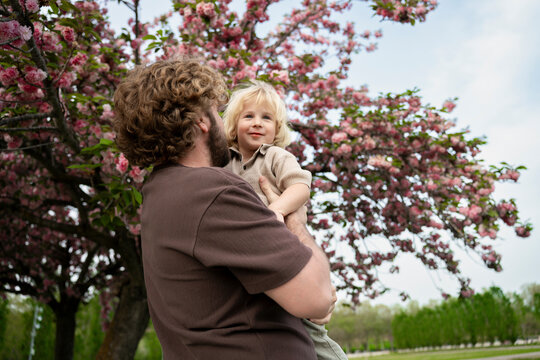 Father holding kid under blooming tree in spring