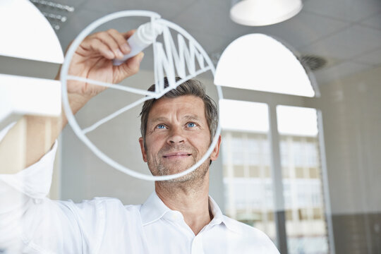 Businessman drawing diagram on glass pane in office