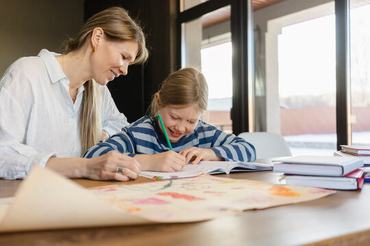 Smiling mother helping daughter doing homework at desk