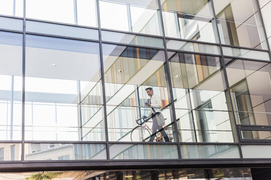 Businessman with cell phone pushing bicycle in office passageway