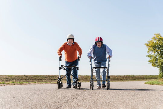 Two old friends wearing safety helmets, competing in a wheeled walker race
