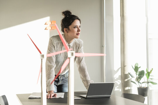 Businesswoman with wind turbine models and laptop on desk in office