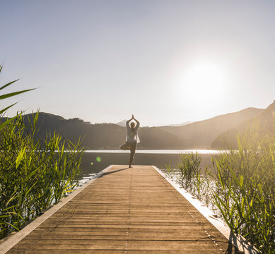 Woman practicing tree pose on jetty by lake