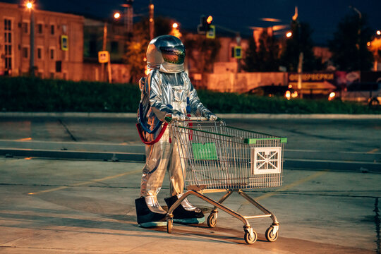 Spaceman in the city at night on parking lot with shopping cart