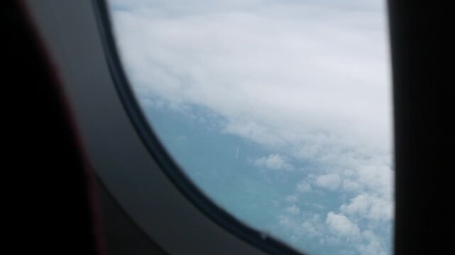 view through airplane window above the clouds and sky inspiration concept in cinematic aerial flying over white fluffy cloudscape in high altitude sky with fresh clean air and blue skies