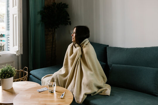 Sick woman looking away while wrapped in blanket at home