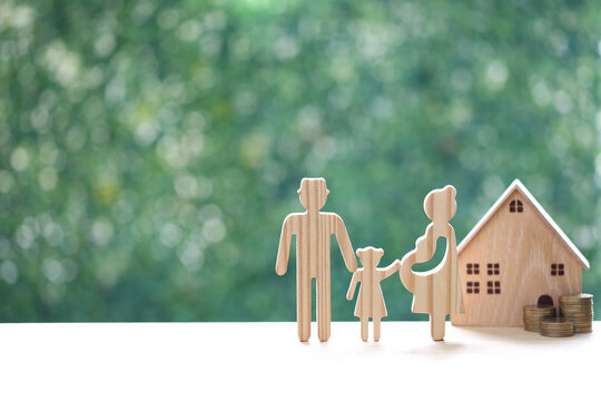 Wooden family figure set including a pregnant mother, father, and daughter standing next to a small wooden house and stacks of coins, symbolizing family growth and financial planning for a home.