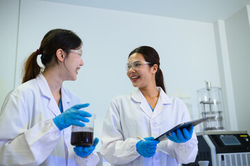Fototapeta premium Two Happy Asian Female Scientists Collaborating in Laboratory with Beaker and Clipboard