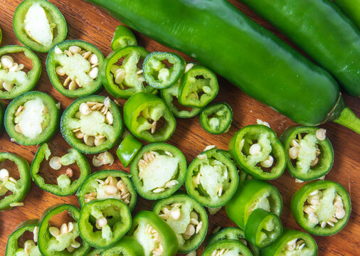 Sliced jalapeno and whole peppers on wooden chopping board. Green chili pepper. Capsicum annuum. top view