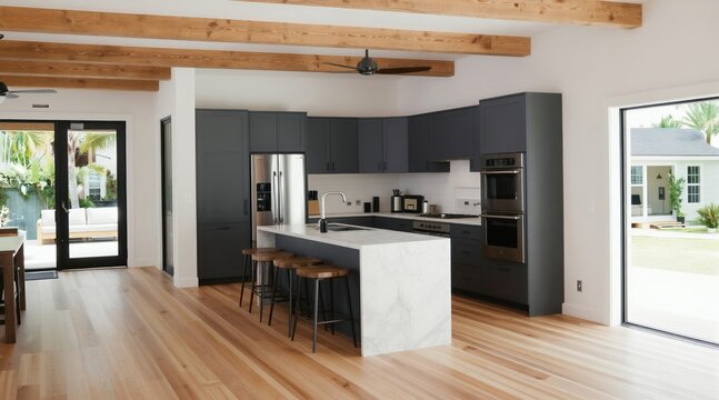 Modern open concept kitchen, living space features dark cabinets marble island, wood floors. Large windows offer backyard views, natural light. Exposed beams add architectural detail to ceiling.