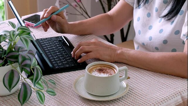 A close-up image of a young woman working on a tablet computer in a cafe.

