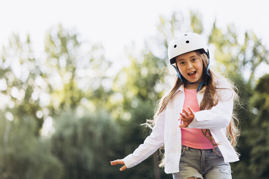 Young girl safely enjoying outdoor rollerskating activity. Childhood recreation in a summer park with protective gear