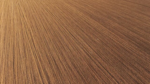 Aerial view of tilled field with diagonal furrows and tractor marks across dry soil surface. Plowed farmland showing clear machinery tracks and organized ground structure. Farming activity with soil