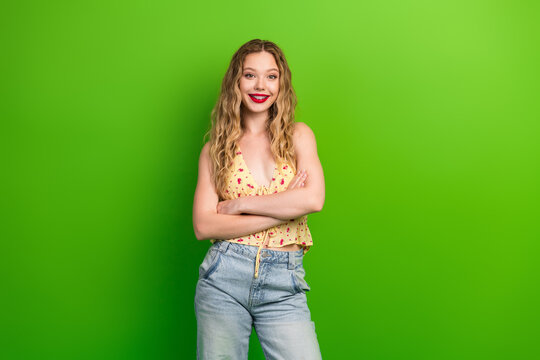 Casual stylish young woman with blonde hair posing in front of green background smiling confidently for lifestyle fashion image