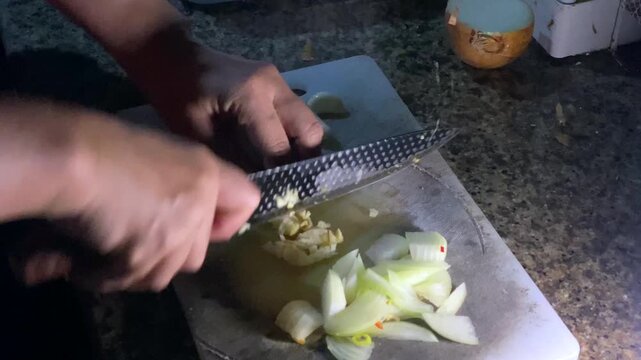 Close-up of hands chopping fresh raw ingredients on a cutting board.
It features a person's hands skillfully slicing and chopping fresh raw ingredients on a rustic cutting board using a sharp kitchen.