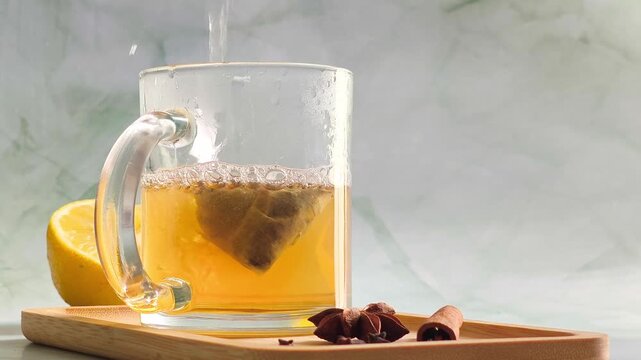 Hand pouring boiling water into clear glass cup over tea bag, dramatic steam and orange color infusion swirl close up