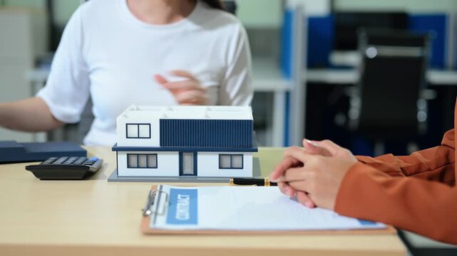 Asian businesswomen discussing real estate investment, home purchase planning and property consultation with house model in a modern office