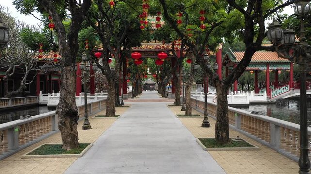 Drone flight through trees filled with red lanterns in temple complex of classic Chinese garden in Guangzhou