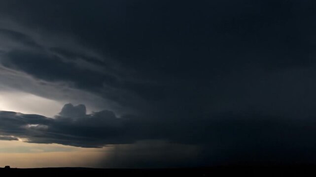 Dramatic storm clouds gather and darken over a flat landscape.