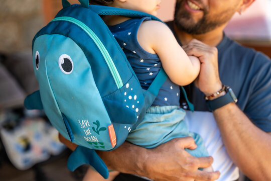 Father holding son with a shark backpack picking up from school