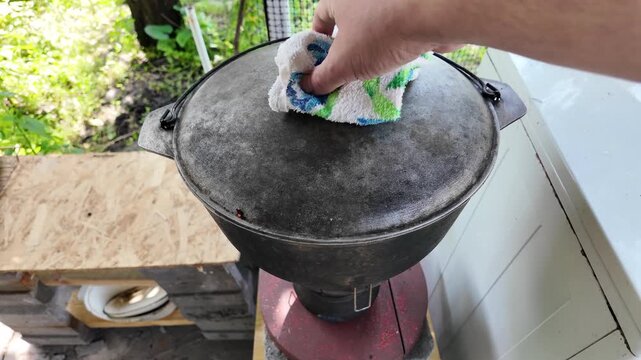 Male hand stirring hot boiling meat stew with a spoon in a large cast iron cauldron outdoors. Traditional rustic camp cooking.