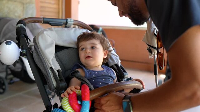 Loving father carefully fastening the safety belt on his adorable baby girl sitting in a modern stroller, ensuring her security before taking a walk together for quality family time
