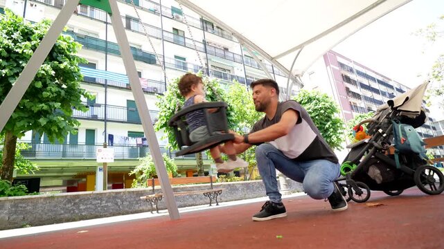 Loving father playfully pushing his happy toddler on a swing in a city park, sharing a joyful moment and bonding together outdoors. Quality family time and active childhood concept