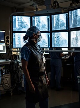 Female cardiologist in lead apron watching angiography screens in a cath lab