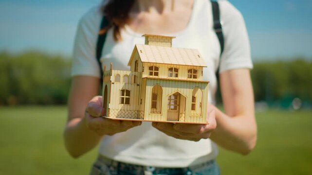 Home ownership proposal with miniature cottage presented forward. Housing loan offer and suburban property purchase concept with relocation planning symbolism. Real estate service and family residence