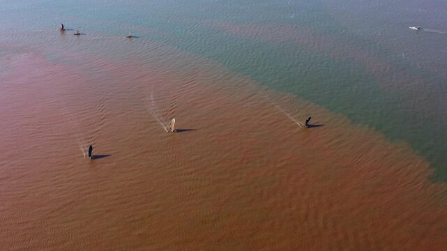 Aerial drone perspective tracking traditional Malagasy boats sailing through contrasting reddish river sediment and green ocean water in Mahajanga.