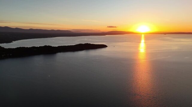 Aerial view of wooded peninsula at golden hour, calm lake, Andes silhouette.