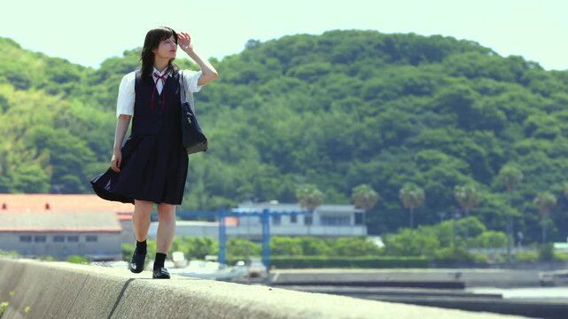 海辺の防波堤を歩く女子高校生と夏の青空