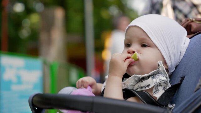baby in stroller eating green apple slice outdoors