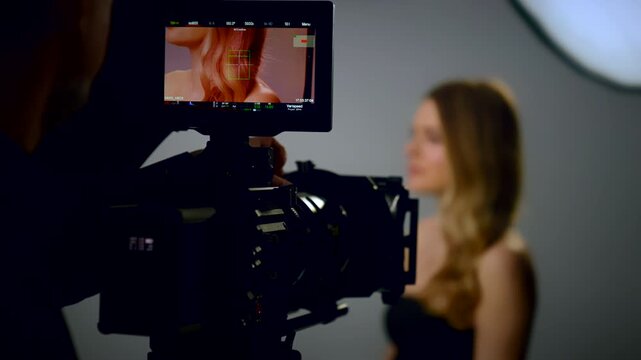Filming in a professional film studio. Female model posing as the camera operator records the video. Selective focus