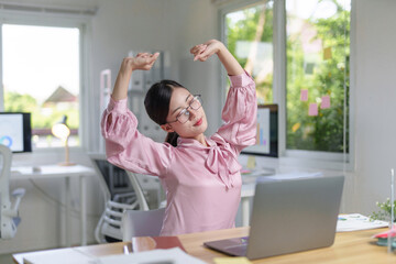 Asian businesswoman stretching arms, relieving fatigue, and relaxing during a short break from work at her modern office © amnaj