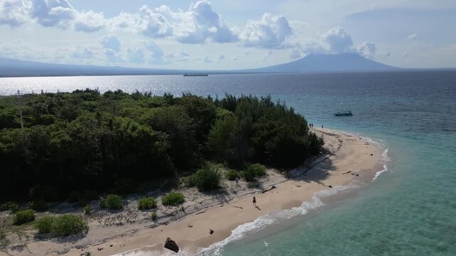Tabuhan Island, East Java aerial zoom out of island and beach with volcano and boat visible in background