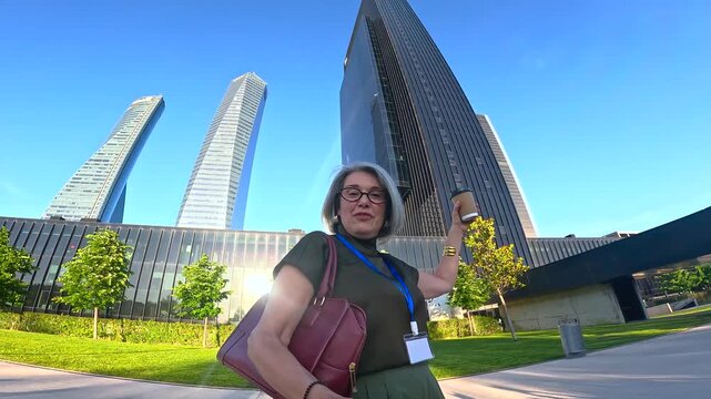 Mature businesswoman with coffee dancing and walking near citylife skyscrapers in milan, enjoying a break outdoors
