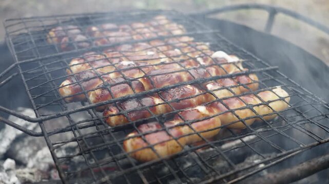 Sausages sizzling on a barbecue grill over hot coals with smoke rising