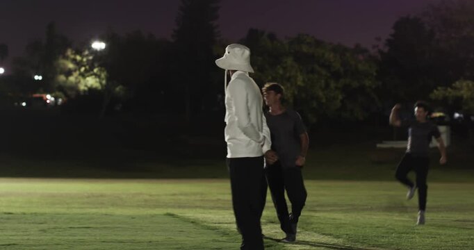 Joggers greeting prompts diverse male partners by floodlights, exchanging bat, preparing for match