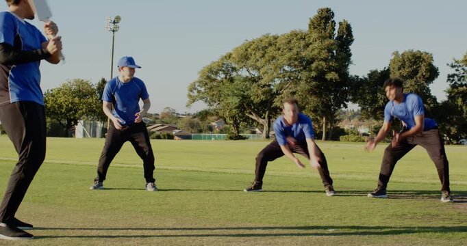 Diverse male teammates in sportswear practicing cricket on cricket pitch, with cricket bat, ball