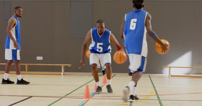 Coach cueing drill, adult african american man dribbling basketball through cones on court
