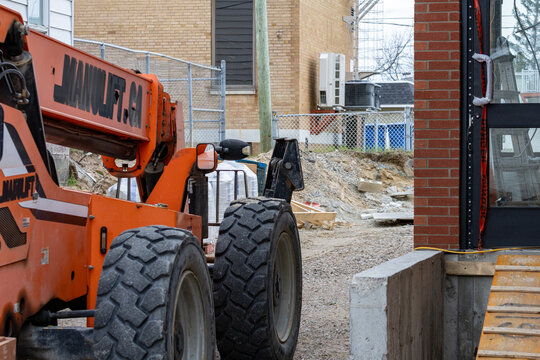 La Tuque, Quebec, 16 May 2026 : Orange Manulift telehandler heavy equipment stands on a construction site next to a new brick building.