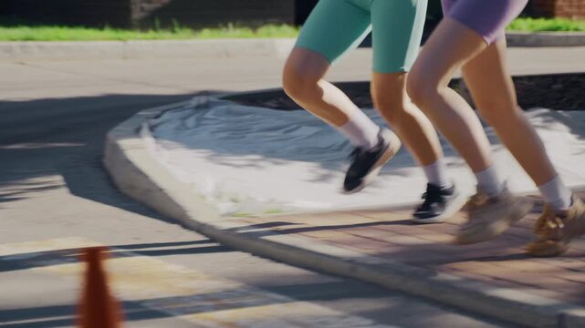 Anonymous athletic twin sisters in bright sportswear running in sync during an outdoor fitness workout in summer