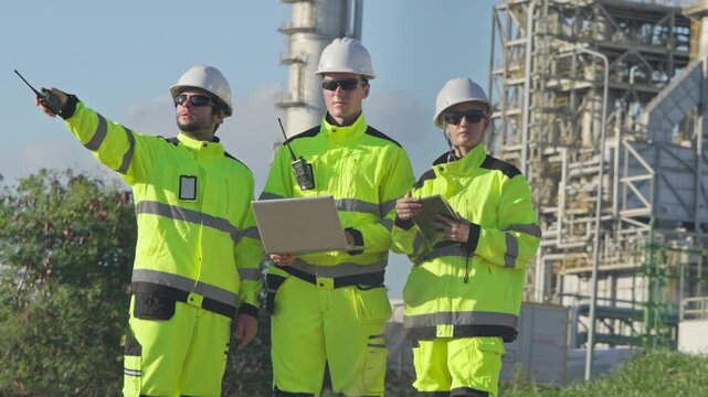 Industrial workers discussing safety protocols oil refinery site digital content outdoor environment wide angle view collaboration insight