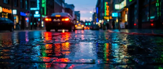 Wet urban street at dusk reflects neon lights from storefronts and vehicles, creating vibrant bokeh effects. Suitable for backgrounds, city themes, and nightlife concepts. © Yuliia