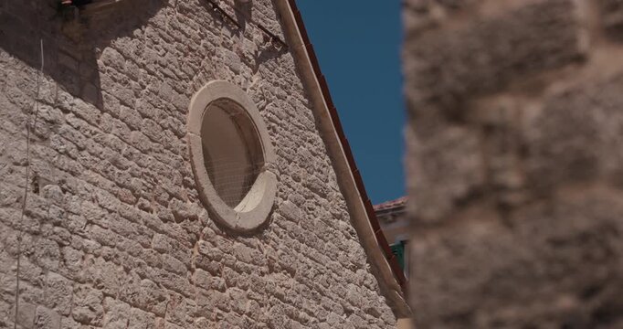 A historic stone facade with a circular window is visible in the old town of Sibenik Croatia.