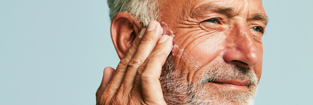 Senior man applying moisturizing cream to his face. Mature male grooming and skincare routine. Healthy aging concept