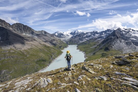 Mountaineer on the summit of Mont de la Blana, view of a blue mountain lake, Lac des Dix reservoir, behind mountain peak Mont Blanc de Cheilon with glacier, H&eacute;rm&eacute;nence, Valais Alps, Valais, Switzerland